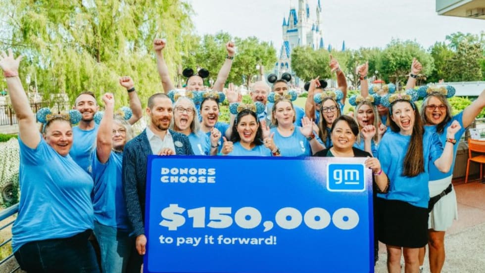Adults in blue shirts holding  a banner with headline $150,000 with Disney World castle in the background.