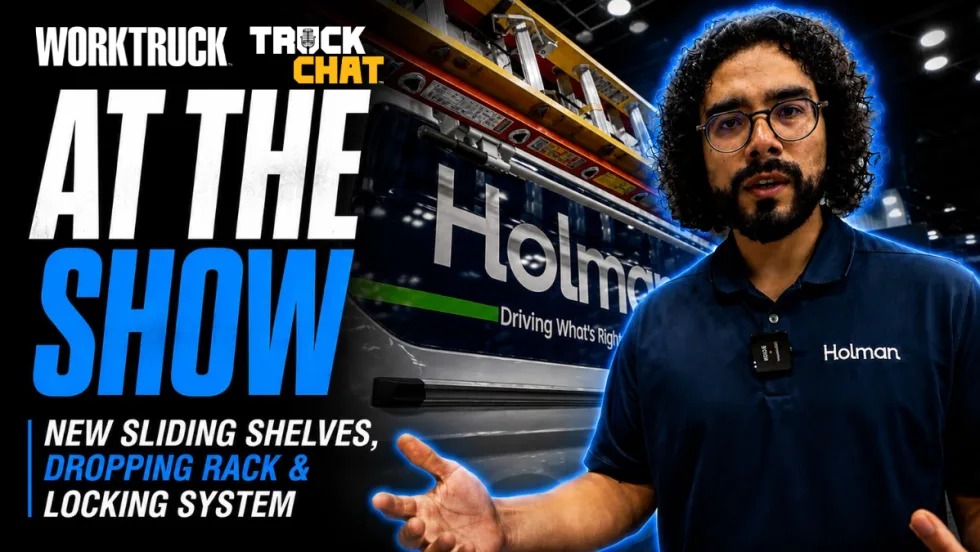 Holman representative standing in front of a commercial work van display at a trade show while discussing new van upfit products, including sliding shelves, ladder rack systems, and locking solutions.
