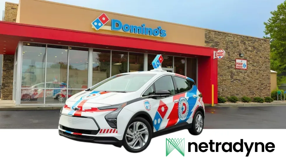 Domino’s-branded electric delivery car parked outside a Domino’s restaurant, featuring red, blue, and white graphics. The image includes the Netradyne logo in the lower corner and storefront pickup signage in the background.