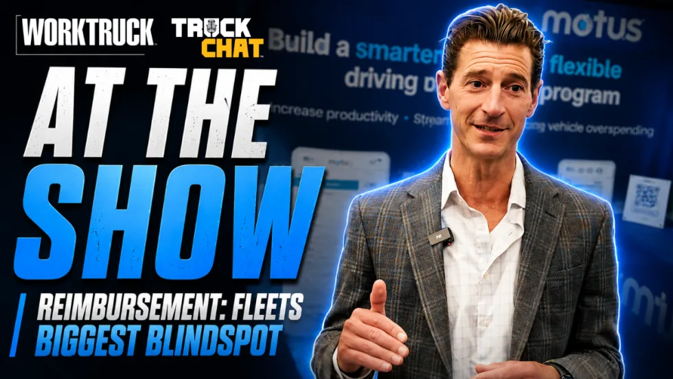 YouTube thumbnail for Work Truck’s Truck Chat series. Large headline text on the left reads “AT THE SHOW” with a subheadline, “Reimbursement: Fleets Biggest Blindspot.” On the right, a man in a gray plaid blazer and white shirt speaks while gesturing with his hand, wearing a wireless microphone clipped to his jacket.