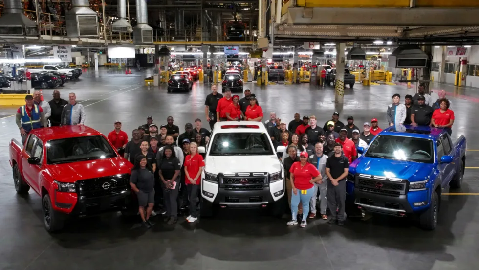 Nissan manufacturing employees gather around red, white, and blue Frontier pickup trucks inside the Canton, Mississippi assembly plant to celebrate a production milestone.
