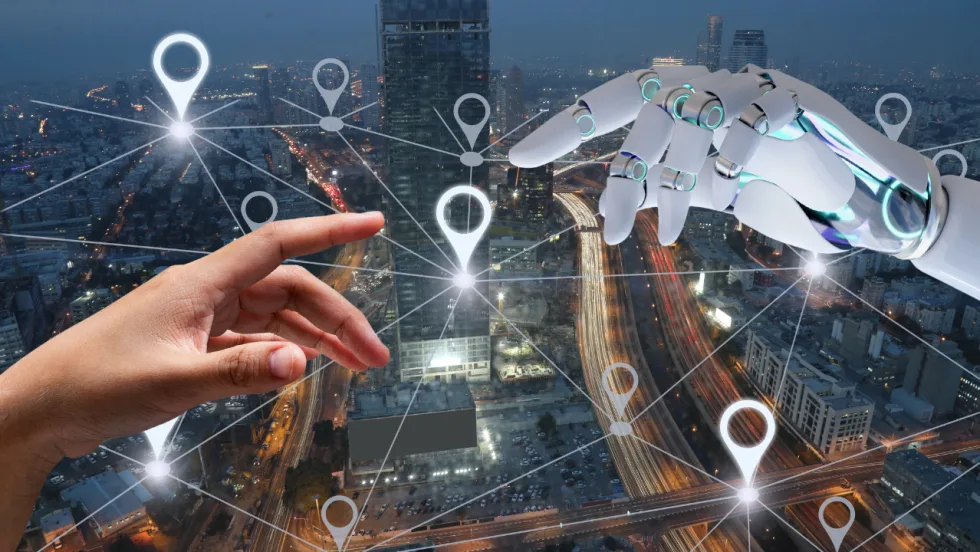 Illustration of a human hand reaching toward a robotic hand over an aerial view of a city at dusk, with interconnected location pins and network lines symbolizing AI, telematics, connected fleet technology, and data-driven transportation.