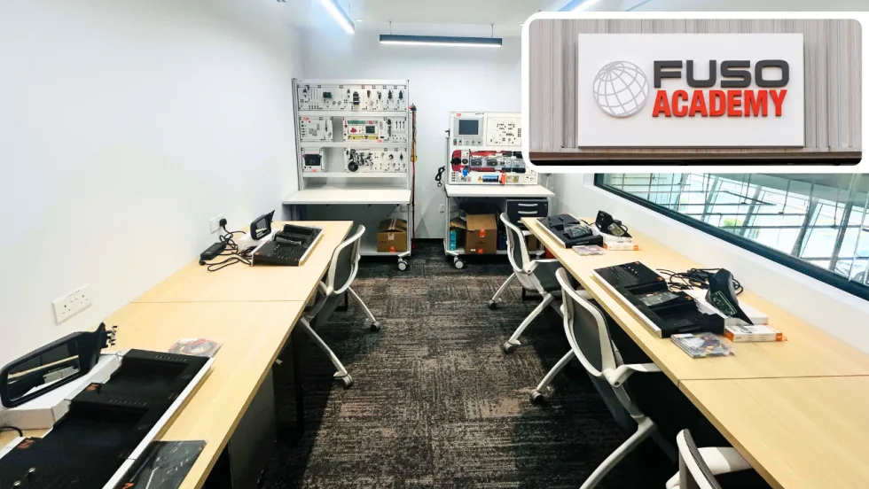FUSO Academy training classroom featuring workstations, diagnostic equipment, and electronics training benches, with a FUSO Academy logo highlighting the company's technical training facility.