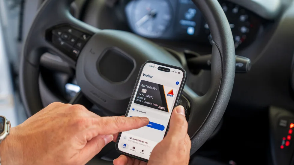 Driver uses a smartphone inside a commercial vehicle to access a digital WEX fleet fuel card in Apple Wallet, illustrating mobile fuel payment and fleet card management technology.