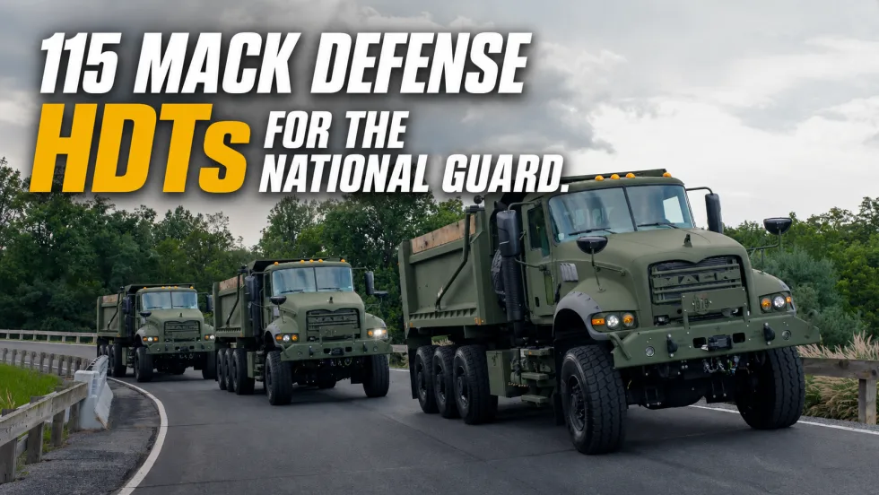 Three olive-drab Mack Defense heavy-duty tactical dump trucks drive in convoy on a roadway beneath cloudy skies, promoting delivery of 115 HDTs for the U.S. National Guard.