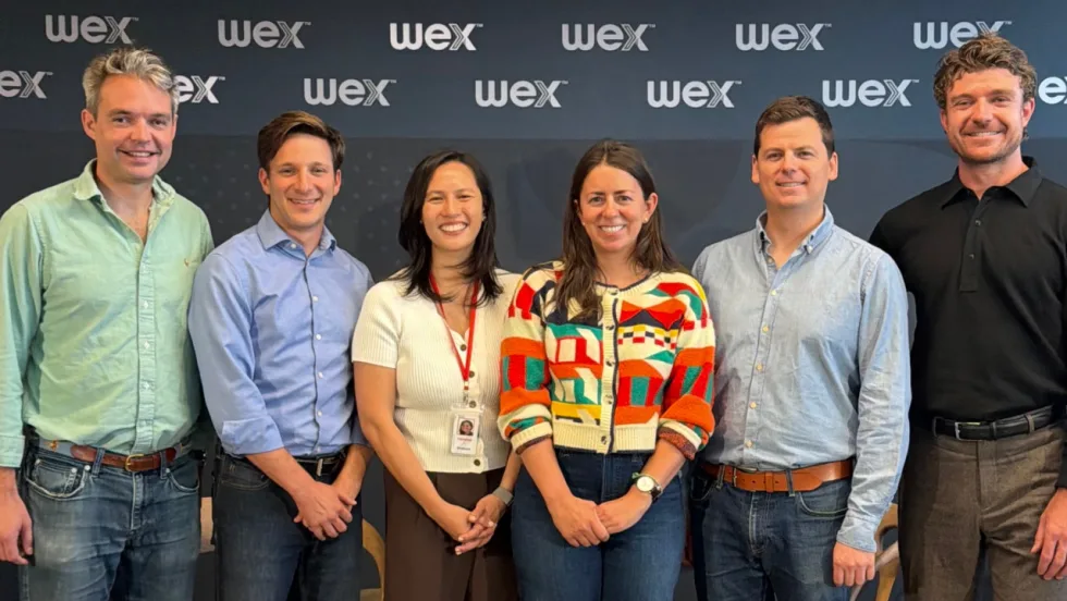 Six WEX and Standard Fleet team members pose together in front of a WEX-branded backdrop, commemorating a business partnership or collaboration between the two companies.
