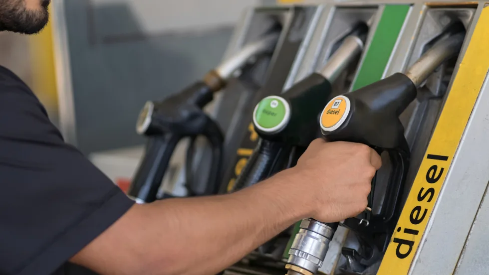 A worker reaches for a B7 diesel fuel nozzle at a commercial fueling station with several fuel options.