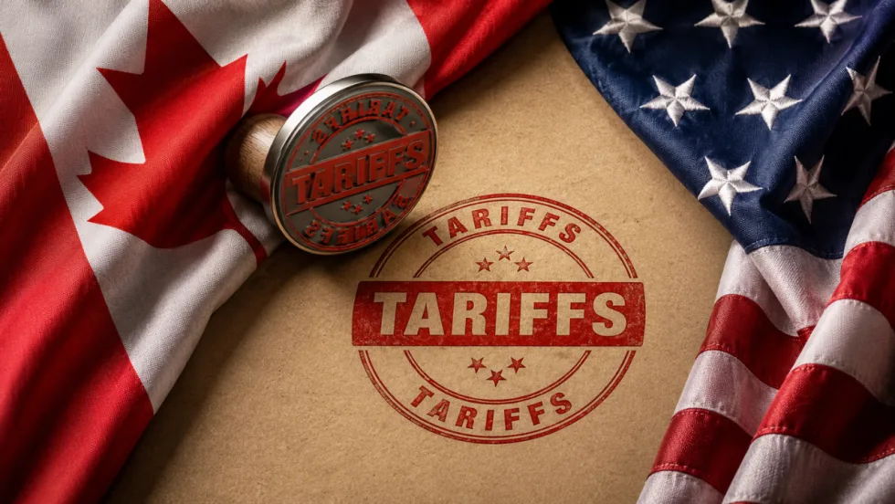 Canadian and U.S. flags frame a red “TARIFFS” stamp on a document, illustrating escalating trade tensions between the two countries.