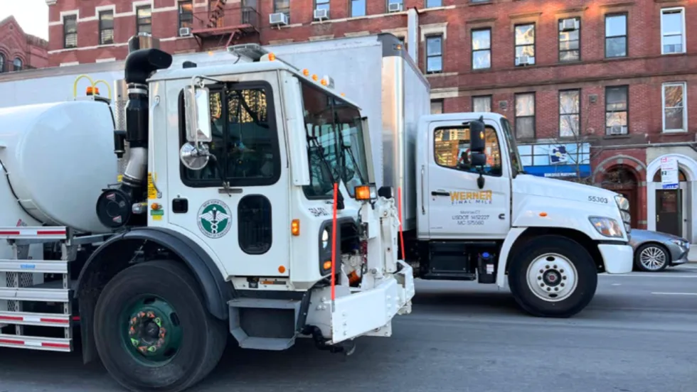 Two commercial trucks, including a municipal service vehicle and a Werner Final Mile truck, parked on a city street in front of brick buildings.