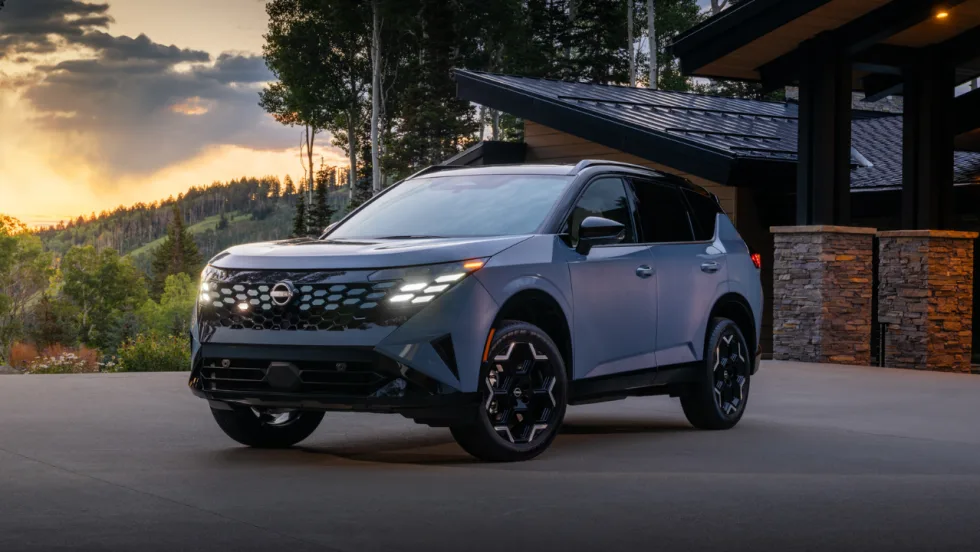 Blue 2027 Nissan Rogue Hybrid parked outside a modern home at sunset, shown from the front three-quarter angle.