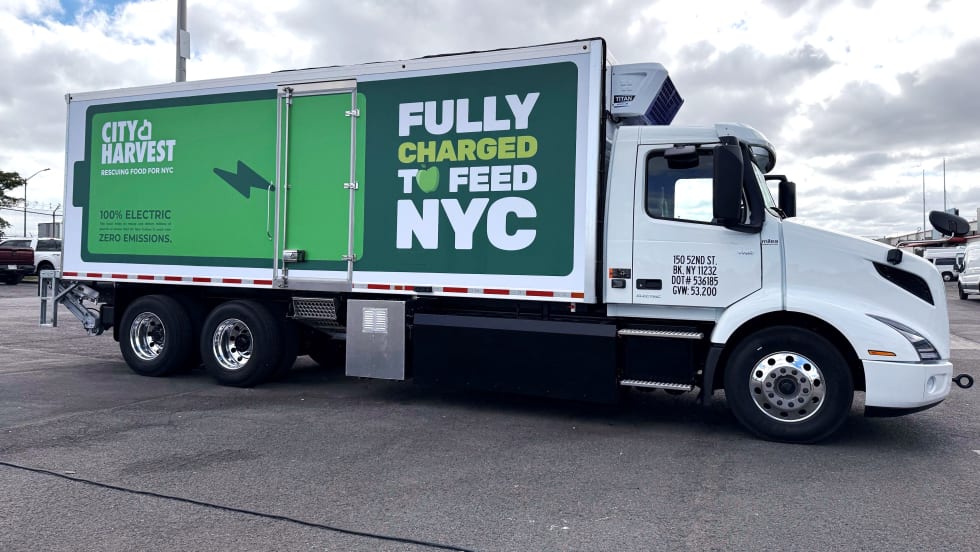 City Harvest Volvo VNR Electric refrigerated box truck featuring green “Fully Charged to Feed NYC” graphics and messaging highlighting 100% electric, zero-emissions operation.