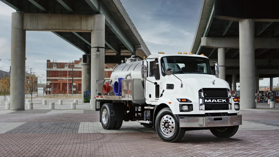 White Mack MD medium-duty vocational truck equipped with a tank body parked beneath an overpass.