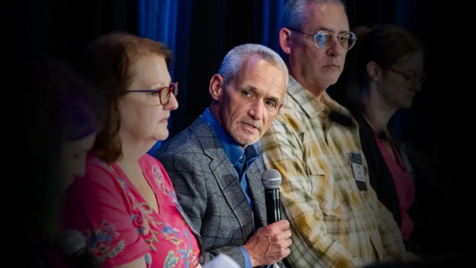 Bob Adamsky, director of fleet management at Arrow International, speaks into a microphone during a panel discussion at Work Truck Exchange, alongside fellow fleet industry professionals.