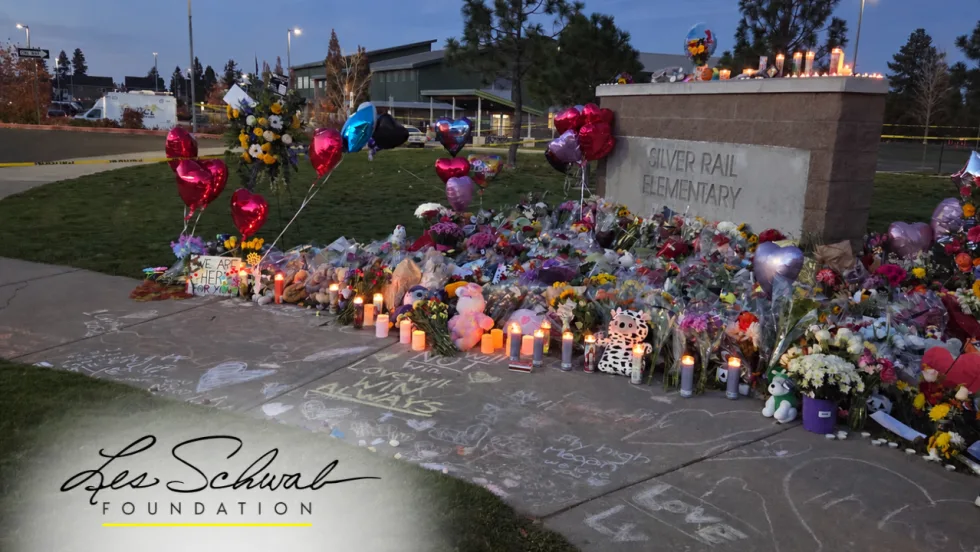 Flowers, balloons, stuffed animals, and glowing candles surround the Silver Rail Elementary School sign at a memorial in Bend, Oregon.