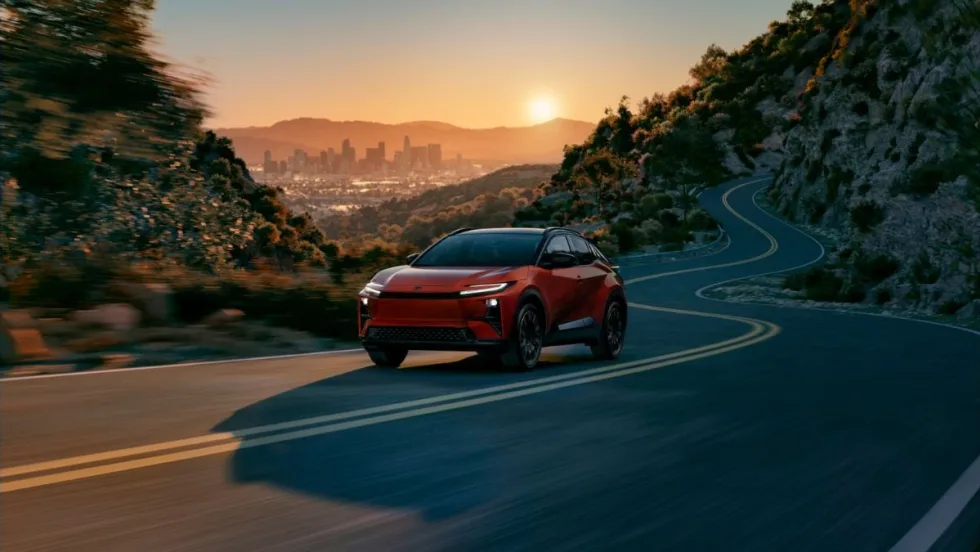 The new 2026 Toyota C-HR BEV driving on a highway with the sunsetting behind it.