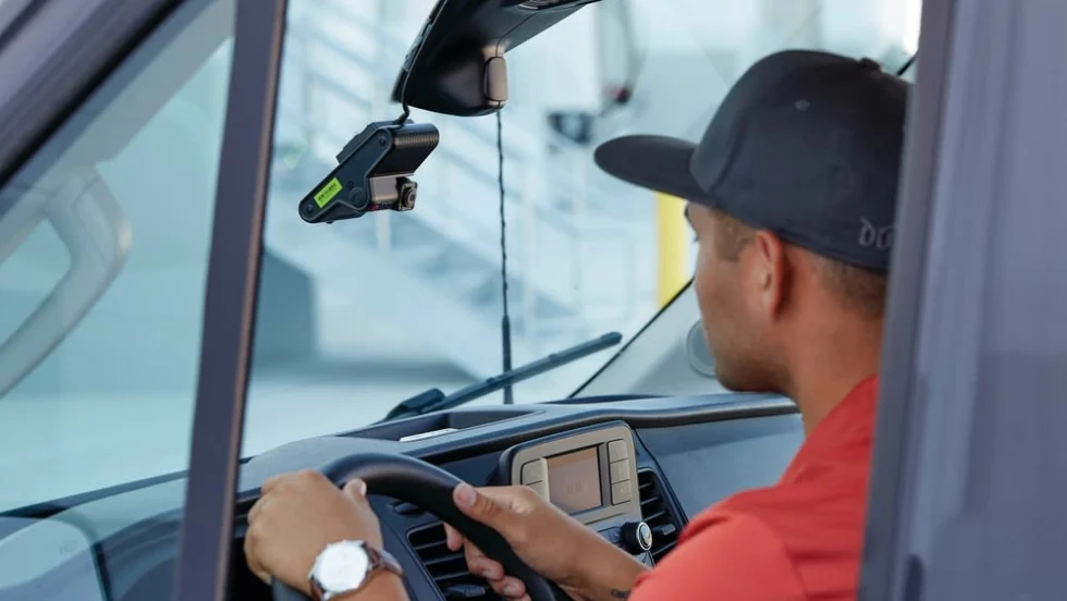 A man in a hat driving in a car with a dashcam overhead