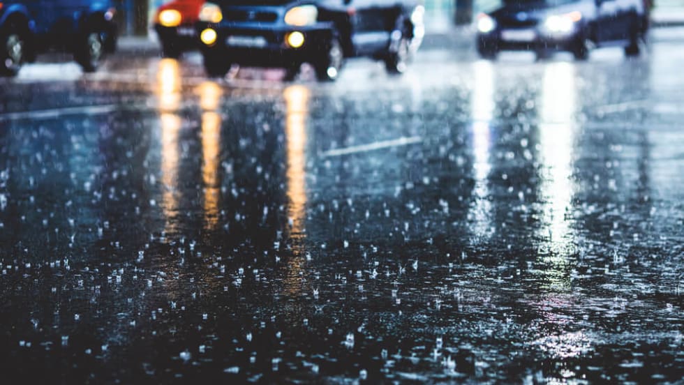 Cars driving through heavy nighttime rain on a reflective road surface depicting hazardous storm conditions that can lead to vehicle damage and insurance claims