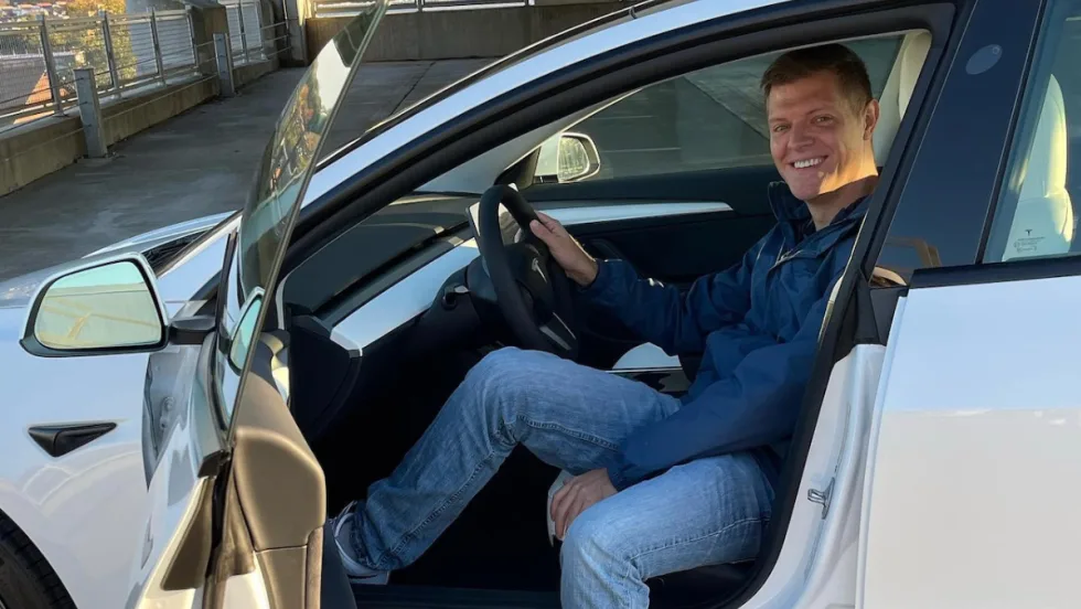 Micah Bergdale sits turned sideways in the driver's seat of a Tesla with the door open.