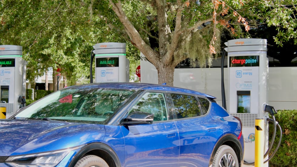 A blue EV backed up against a charging station in a parking lot.