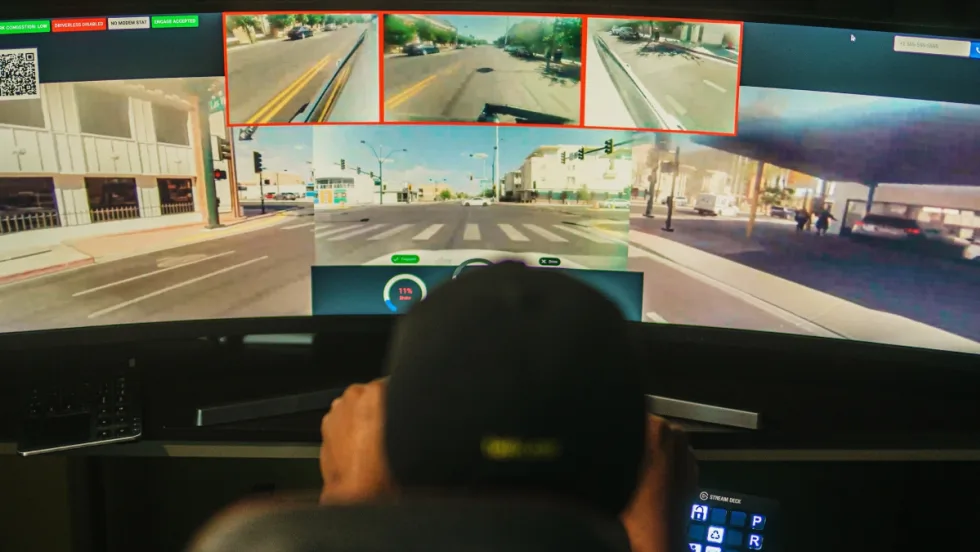 Back view of a remote driver in front of a screen delivering a car to a location.