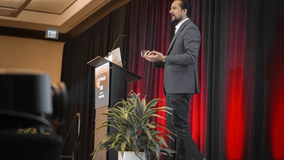 Side view of ICRS speaker Sanchit Garg at podium in front of a floor lit red curtain