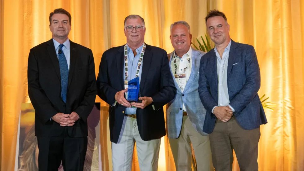 Award winner on stage with presenters in front of yellow curtain.