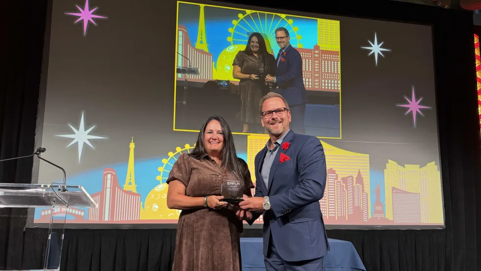 Jamie McKay stands on stage and poses with teh 2026 Fleet Visionary award at AFLA