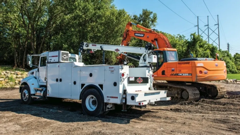  White utility service truck with a crane parked beside an orange excavator at a roadside work site.