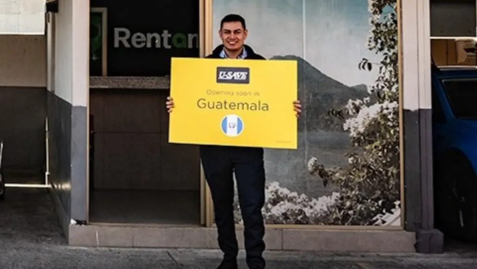 Franchisee standing with yellow U-Save branded sign in front of the rental car outlet.