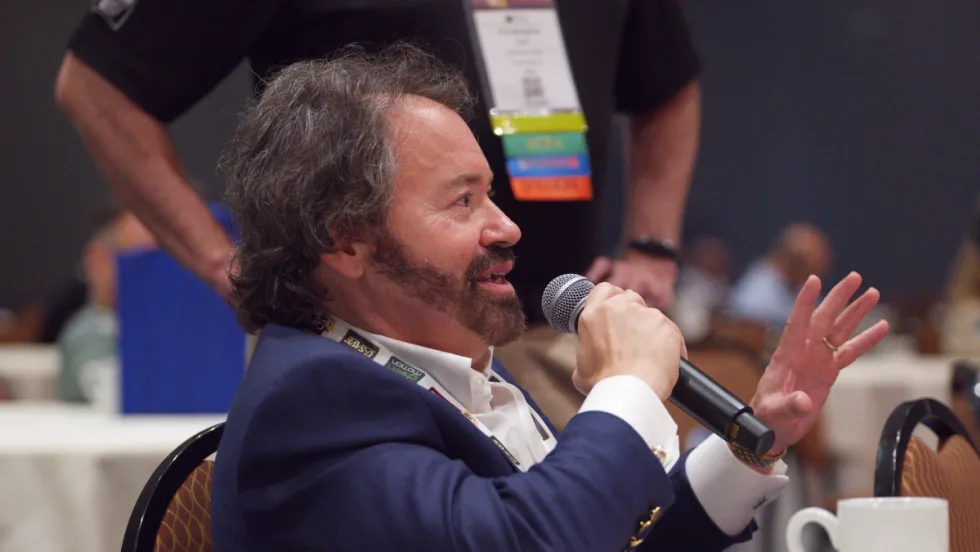John Possumato holding microphone while asking a question during a live conference session at the ICRS Show.
