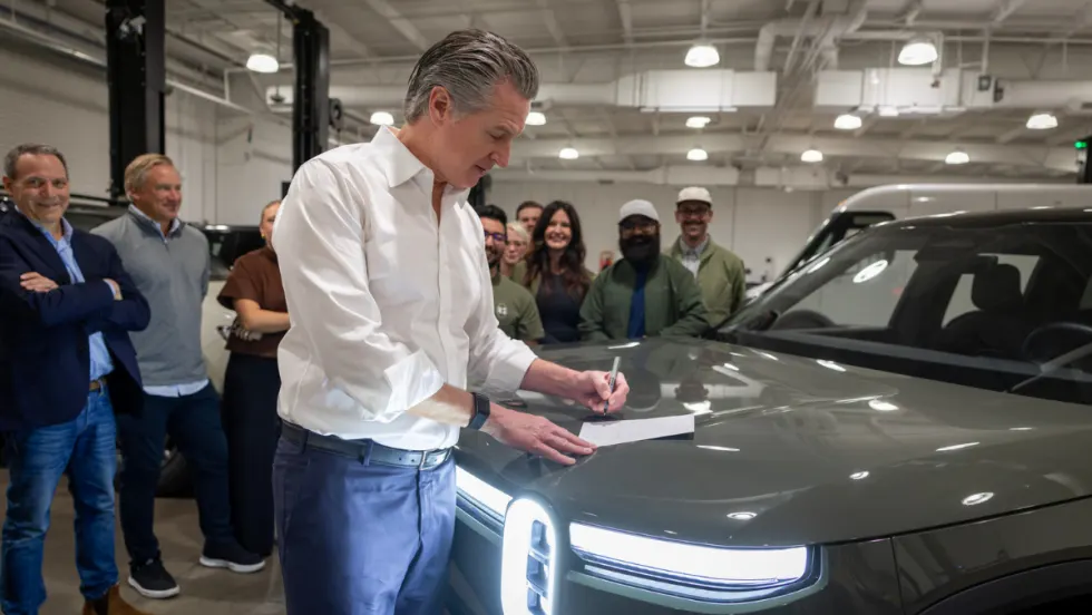 Gov. Newsom signs legislation on the hood of an EV.