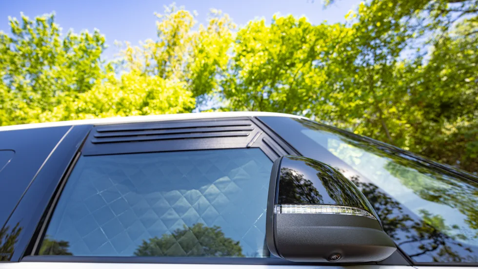 Close-up of the 2027 Volkswagen ID. Buzz side window with quilted privacy shades and integrated side mirror camera parked outdoors.