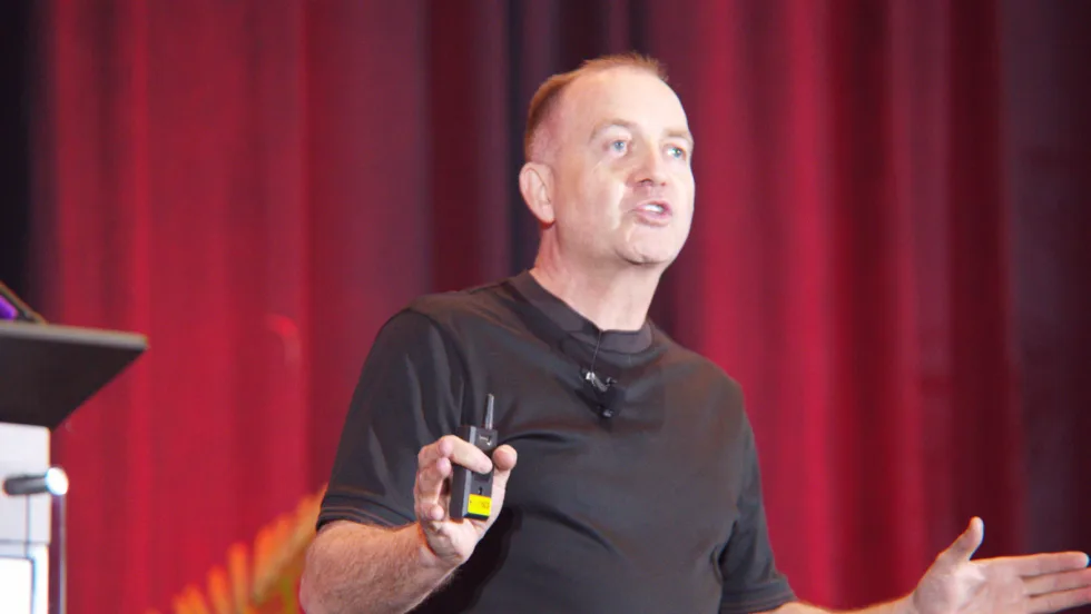 Richard Lowden gesturing on stage in front of a red curtain at the Gaylord Texan Resort near Dallas.