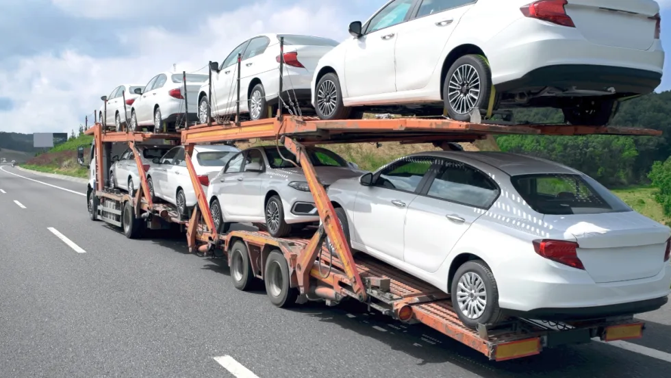 A double-decker stinger car hauler carries a full load of new white vehicles along an interstate highway.