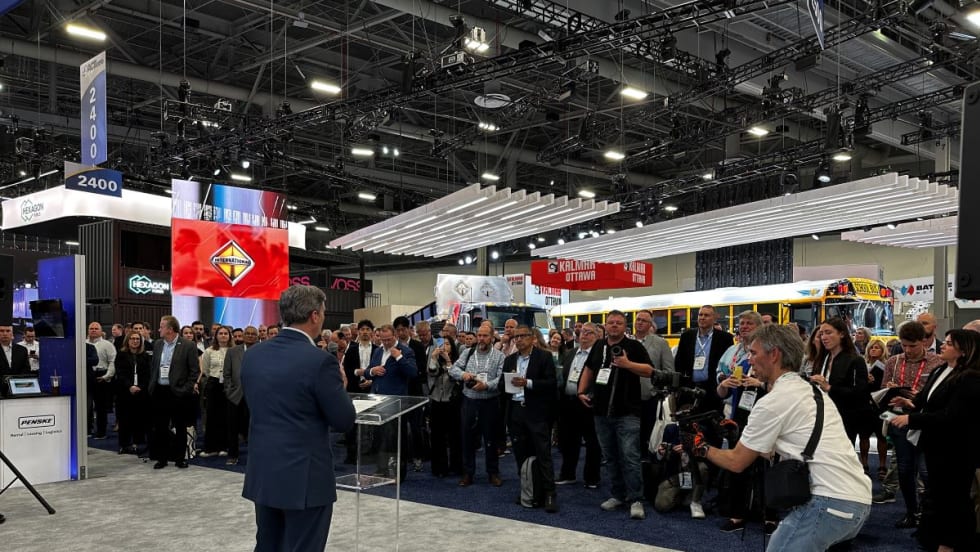 Man standing at podium in expo hall in front of reporters and industry representatives. 