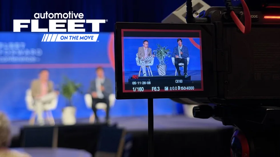 A camera monitor shot of two people on a conference stage. 