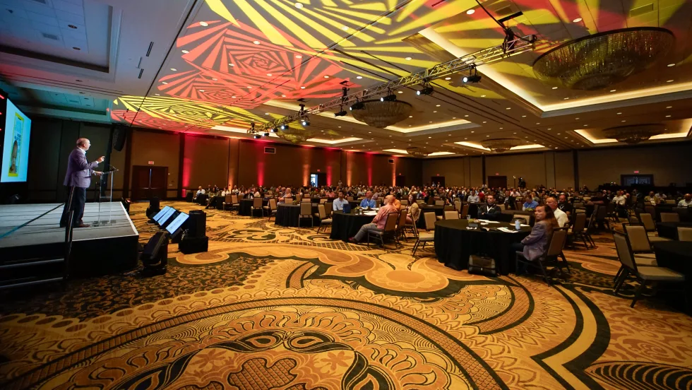 Wide shot of main ballroom with attendees sitting. 