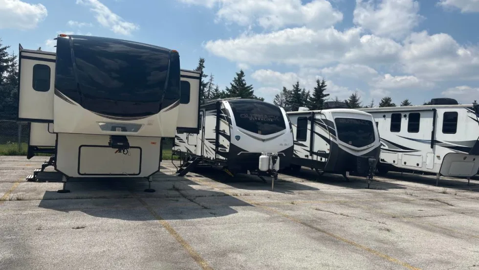 Camper trailers lined up in a parking lot underneath a blue sky with white puffy clouds. 