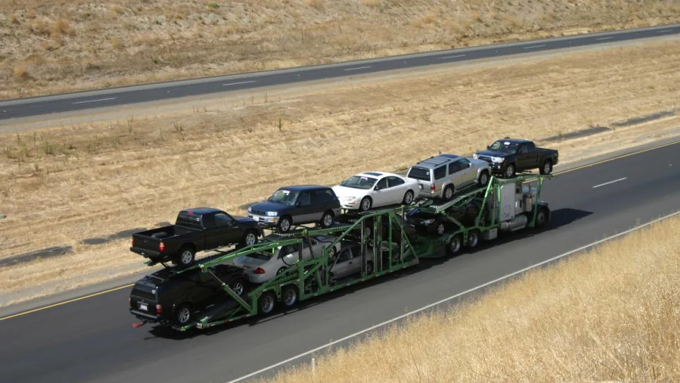 A double-decker stinger truck with a full load of vehicles driving down a rural interstate.
