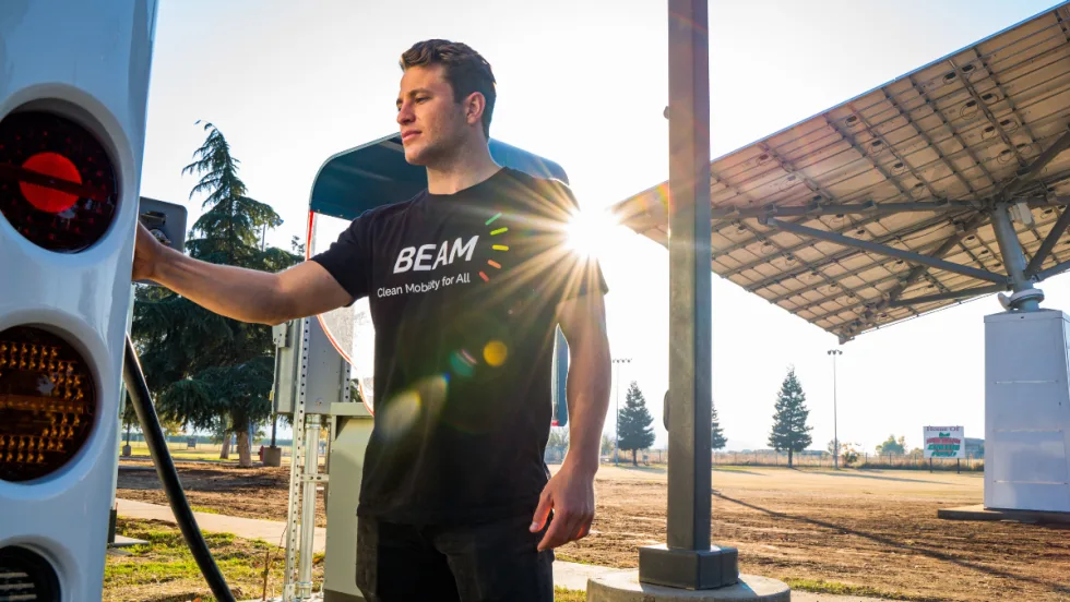 A person uses a Beam Global EV ARC off-grid EV charger next to a solar panel canopy.