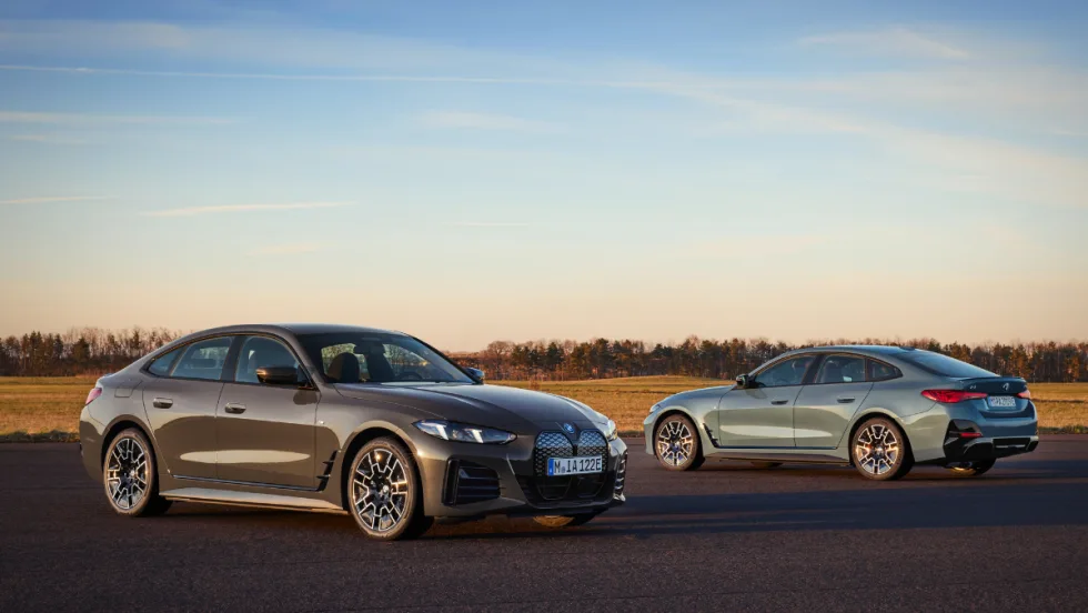 Two BMW i14s are posed on the open road in front of a sunset, with one facing away with a view of the back.