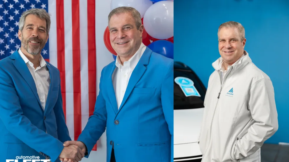 Two business leaders in blue suits shake hands in front of a U.S. flag and balloons, symbolizing AVILOO’s leadership transition and expansion in the North American EV market.