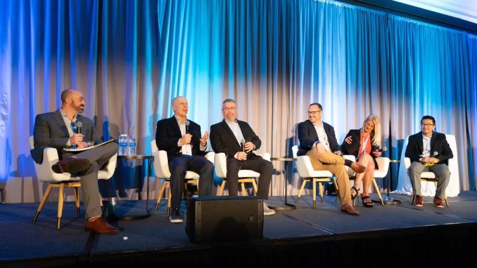 Six panelists on a stage in front of a blue curtain.