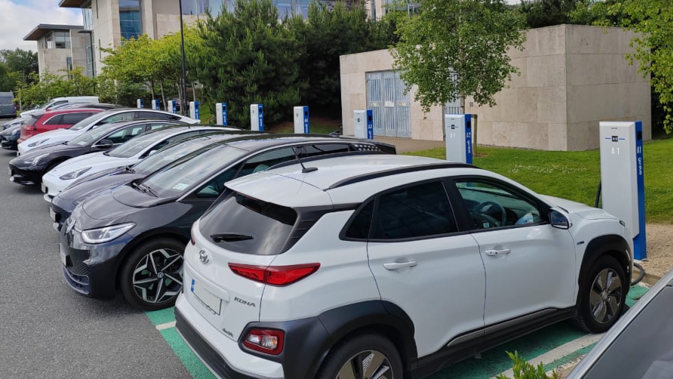 A front view of a row of electric vehicles lined up at parking lot chargers.