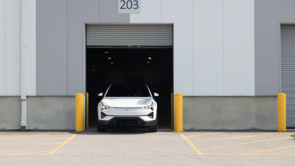 An image of the front end of a white Polestar 3 parking within the open frame of a commercial garage door.