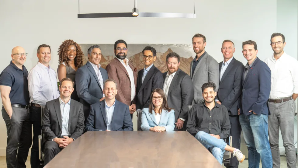 Executives pose around boardroom table.