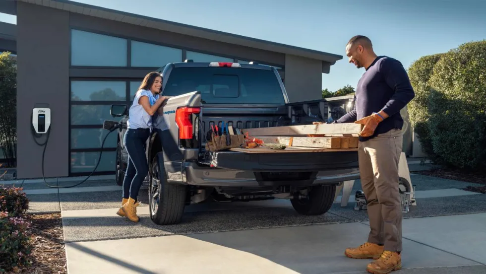 Couple unloading a Ford F-150 electric pickup truck in their driveway.
