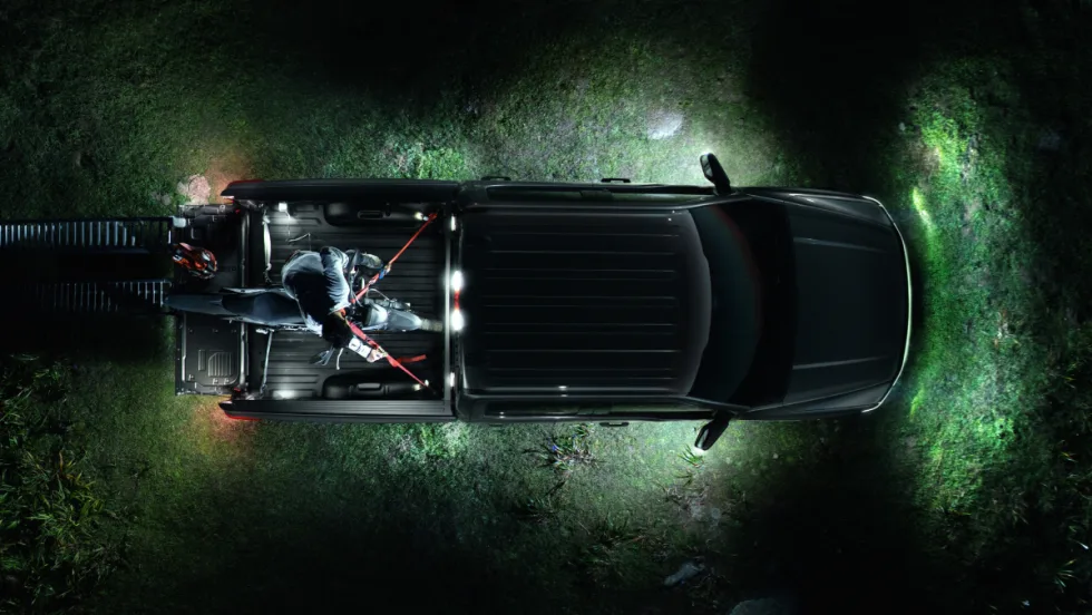 A nighttime aerial close-up of a Ford F-150 Lightning all-electric pickup truck with surround lighting parked on a grass field.
