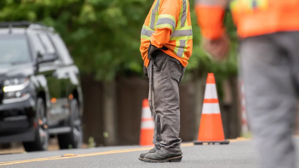 Man standing on the road with a road safety reflective vest on and safety cones on the road. 
