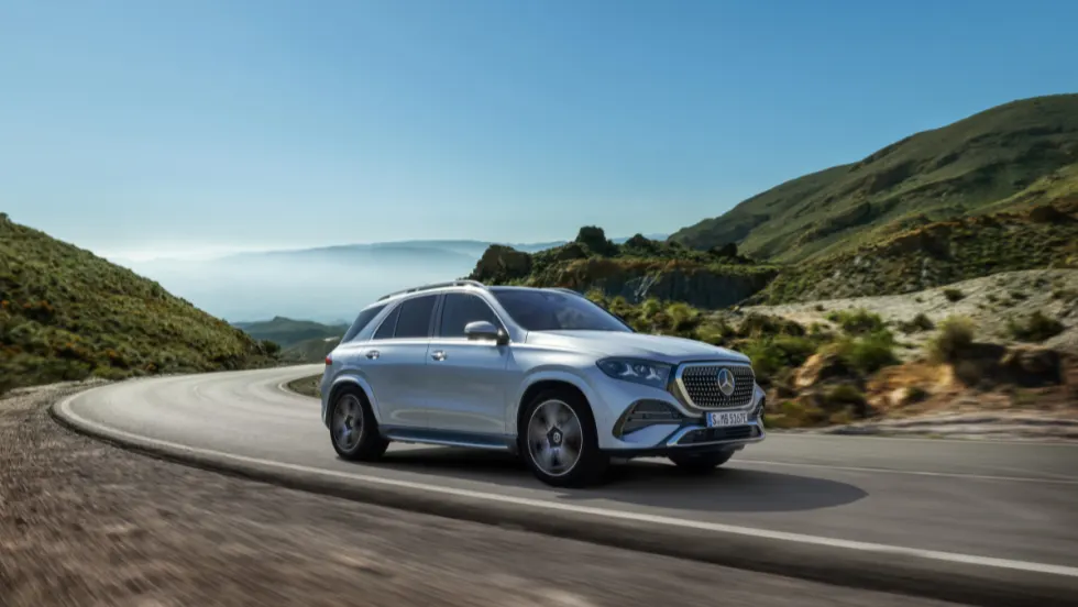 Silver Mercedes-Benz GLE SUV driving on a winding mountain road, showcasing updated exterior design and performance in a scenic landscape.
